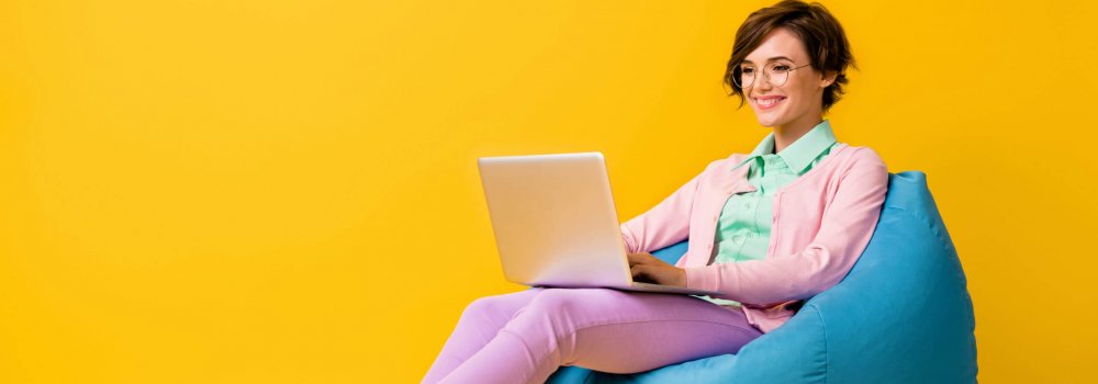 Full length body size photo of female freelancer sitting in glasses working on computer smiling isolated on vivid yellow color background